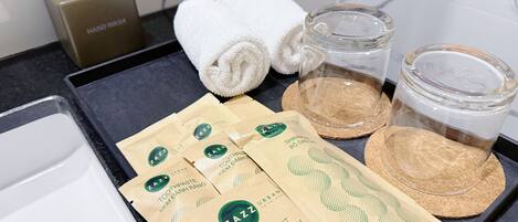 Una encimera de baño con dispensador de jabón líquido, toallas, un tarro de vidrio y bolsas de artículos de aseo.