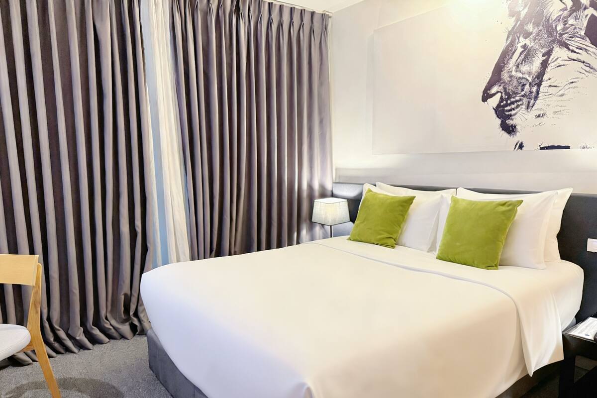 A neatly made bed with white and green pillows, a grey headboard, and a grey curtain in the background.