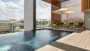 An indoor swimming pool with a view of the cityscape, wooden deck, and lounge chairs. - Zazz Urban Ho Chi Minh Hotel (Ho Chi Minh City)