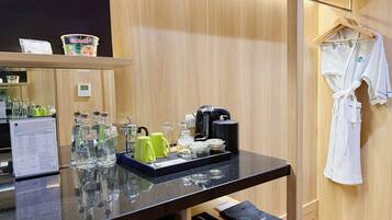 Una camera d'albergo con arredamento in legno, un piano di lavoro nero con diversi oggetti, un accappatoio su un appendiabiti e un tavolino con una borsa nera etichettata 'laundry'.