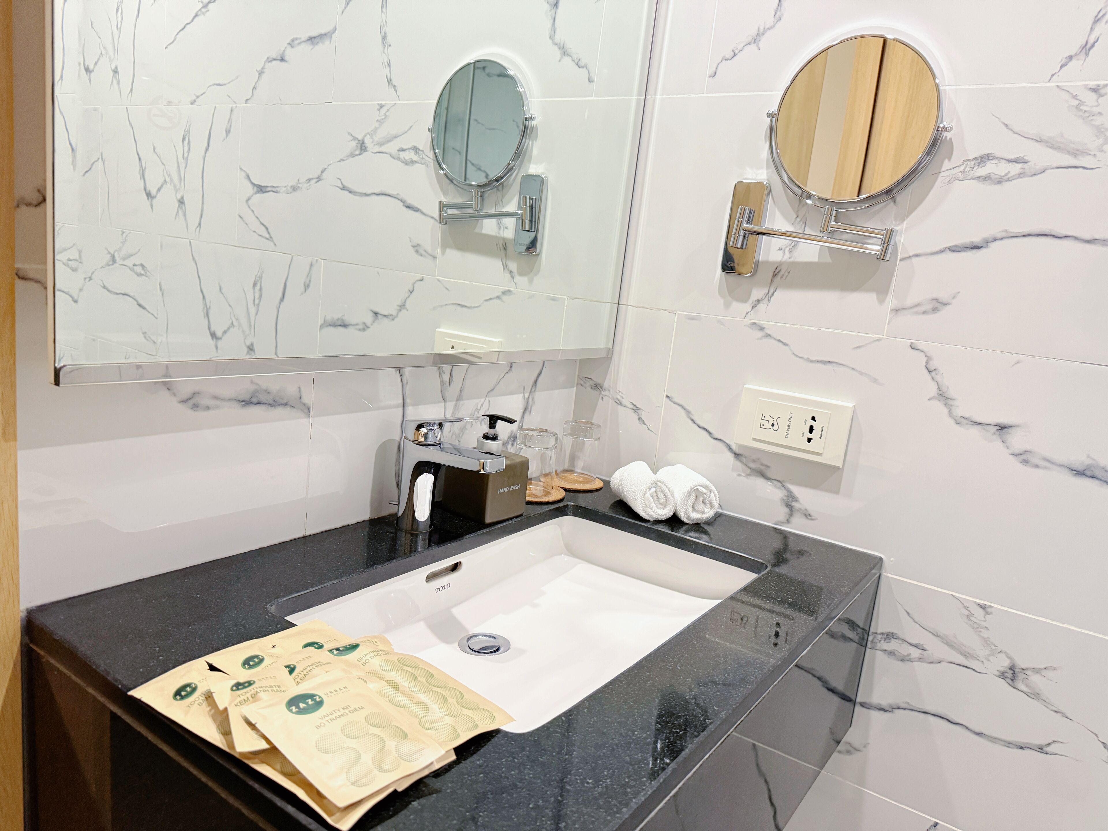 A modern bathroom with a marble backsplash, a black sink, a mirror, and a hand soap dispenser.