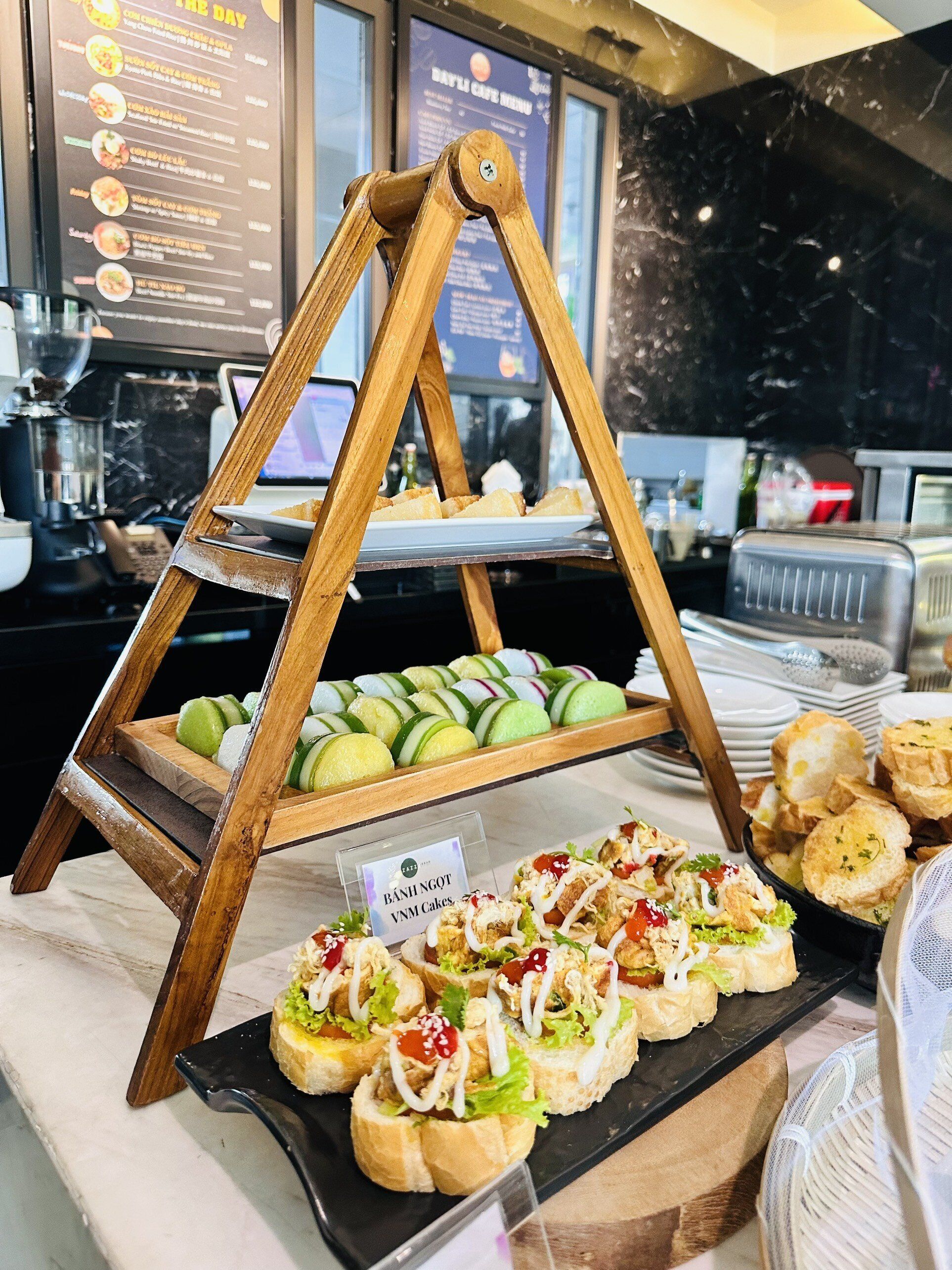 A buffet setup with a wooden stand displaying various food items, including sandwiches and sliced fruits.