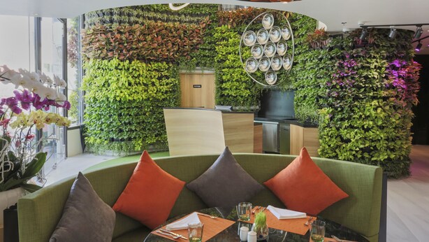 A modern interior with a green sofa, a dining table, and a vertical garden wall. - Zazz Urban Ho Chi Minh Hotel (Ho Chi Minh City)