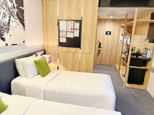 A hotel room with a bed, a wooden wardrobe, a small desk, and a wall-mounted bulletin board.
