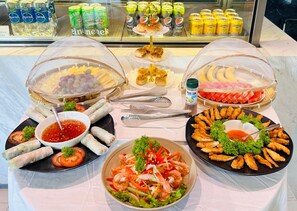 A buffet table with various dishes, including spring rolls, shrimp salad, and fried items, with condiments and drinks in the background. - Zazz Urban Ho Chi Minh Hotel (Ho Chi Minh City)