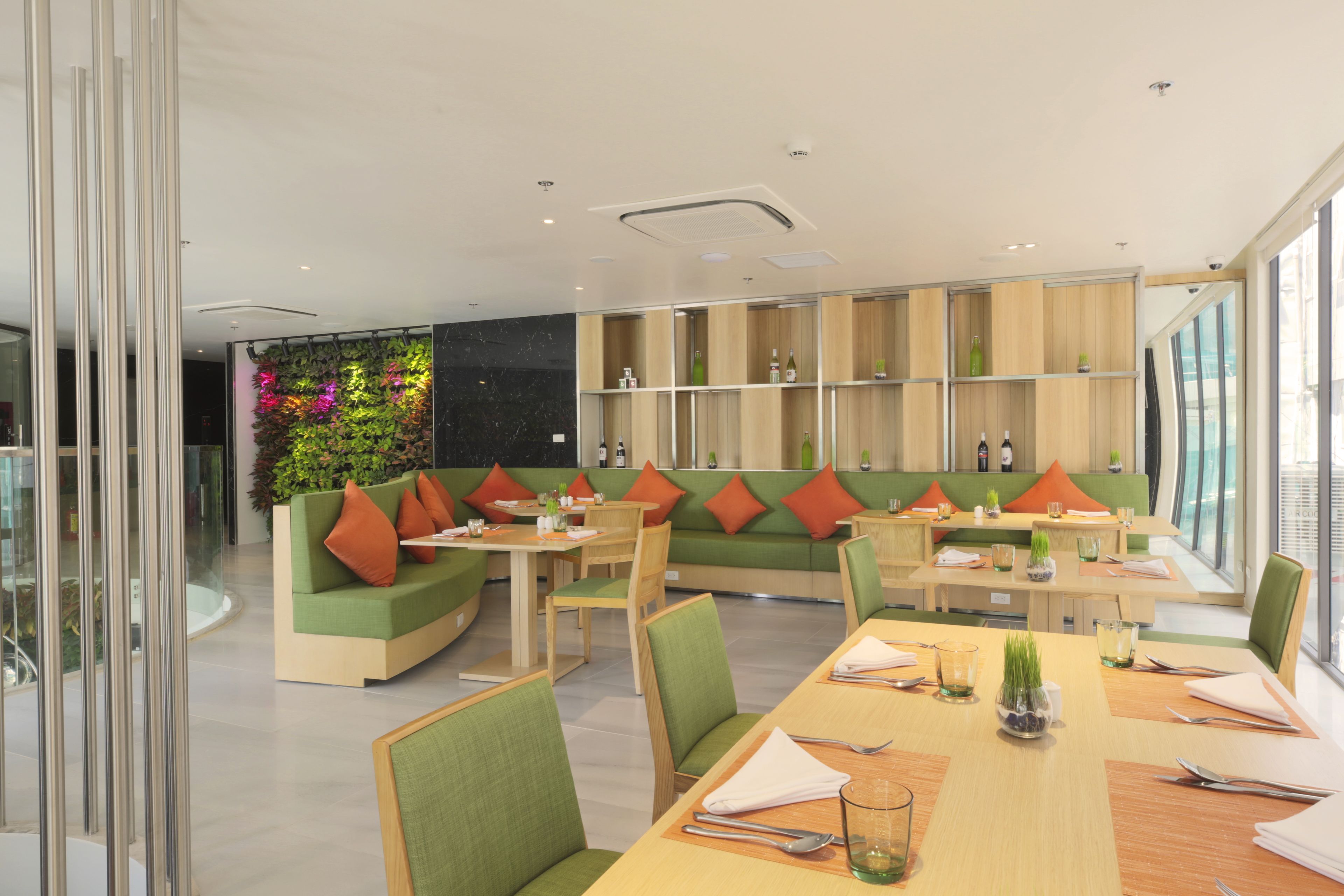 Een modern restaurant met groene zitplaatsen, houten tafels en een decoratieve wand met planten.