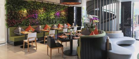 A modern interior with a green sofa, a curved black seating area, and a wall adorned with plants.