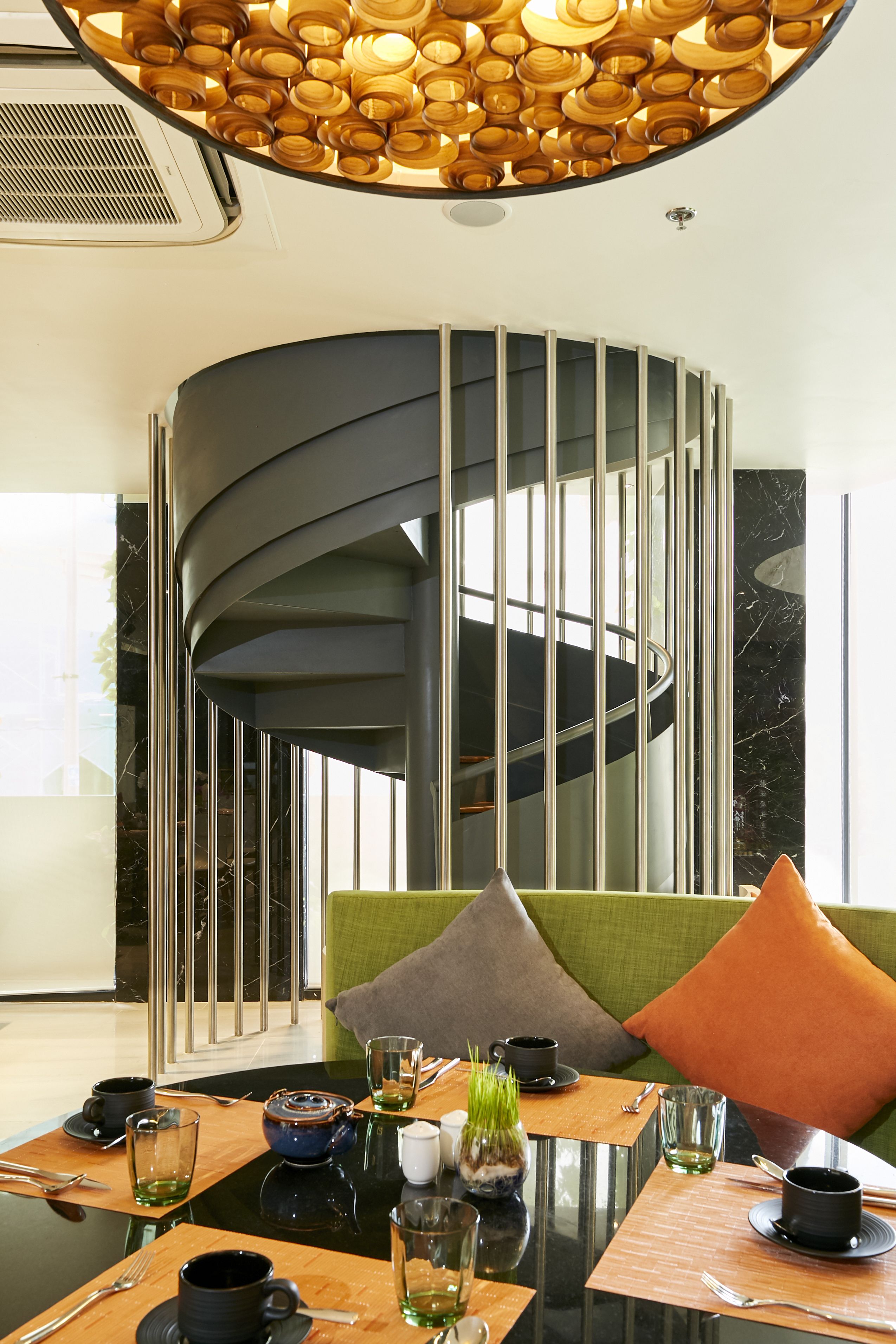 Un espace repas moderne avec un escalier en colimaçon, une table en verre et une variété d’articles de table.
