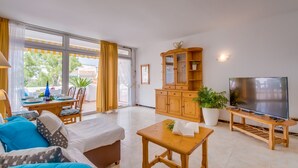 A spacious living area with a sofa, a wooden cabinet, a TV, and a dining table with chairs.