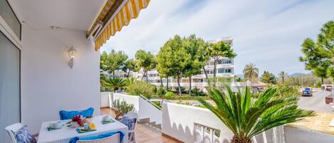 Ein Balkon mit Tisch für zwei Personen, weißen Korbstühlen und einem Blumentopf.