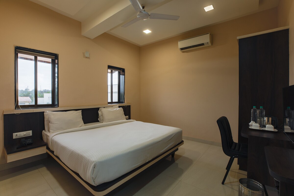 A hotel room with a bed, a desk, a chair, an air conditioner, and a ceiling fan.
