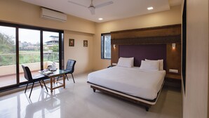 A modern hotel room with a large bed, a desk with a chair, and a balcony with a view of buildings. - City Palace Resort (Mawal)