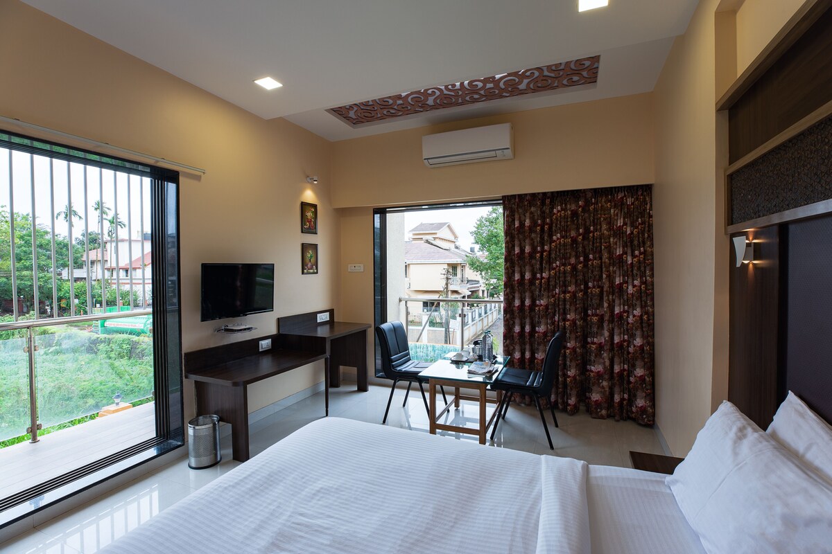 A hotel room with a bed, a desk with a chair, a television, and a balcony with a view of the outside.