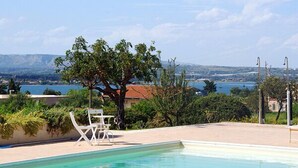 A pool area with a view of a body of water and distant hills. - Sicilian farmhouse from the 19th Century - close to the beach and with a large pool (Siracusa)