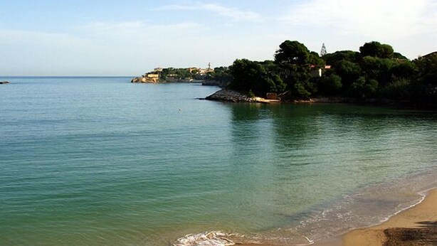 A coastal scene with calm waters, a sandy beach, and a rocky outcrop with trees. - Sicilian farmhouse from the 19th Century - close to the beach and with a large pool (Siracusa)
