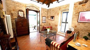 A rustic room with stone walls, a wooden cabinet, a glass table, a striped sofa, and a dining table with plates. - Sicilian farmhouse from the 19th Century - close to the beach and with a large pool (Siracusa)