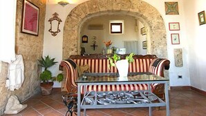 A rustic interior with a stone wall, a wooden ceiling, a stone archway, a striped sofa, a metal table, and a hanging light fixture. - Sicilian farmhouse from the 19th Century - close to the beach and with a large pool (Siracusa)
