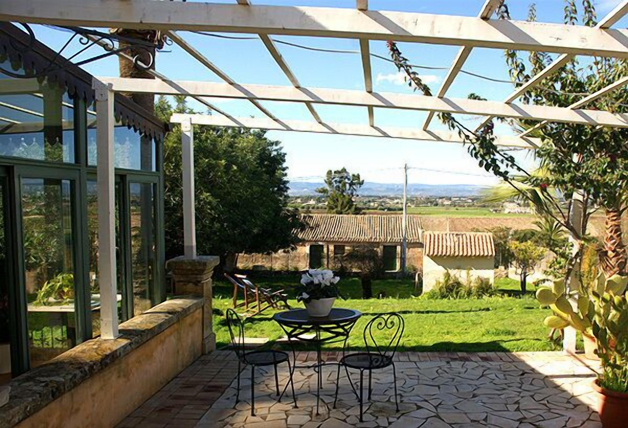A patio with a table and chairs, a pergola, and a view of a rural landscape.