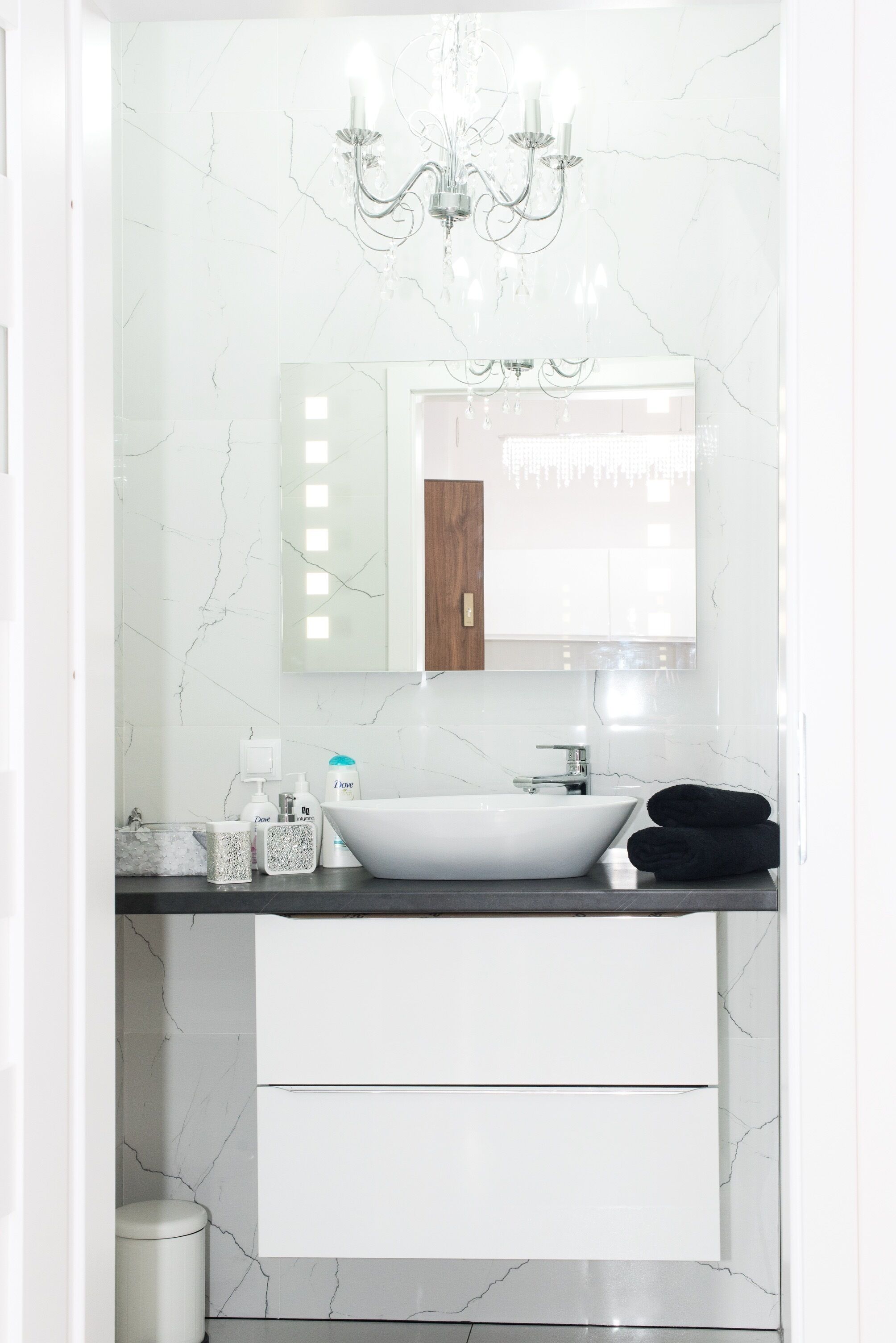 Un baño moderno con un lavabo de mármol blanco, un espejo grande y una araña.