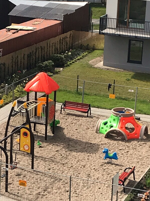 Un parque infantil con una estructura roja para escalar, un juguete motorizado verde y rojo, y un caballo azul con forma de juguete.
