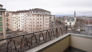 A balcony with a view of a multi-story building and a church in the distance. - PRIMADOM Aparthotel (Geneva)