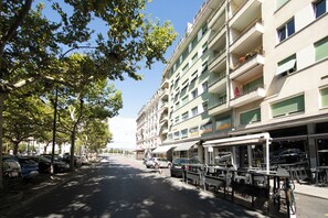 A multi-story building with balconies, a row of parked cars, and outdoor seating. - PRIMADOM Aparthotel (Geneva)