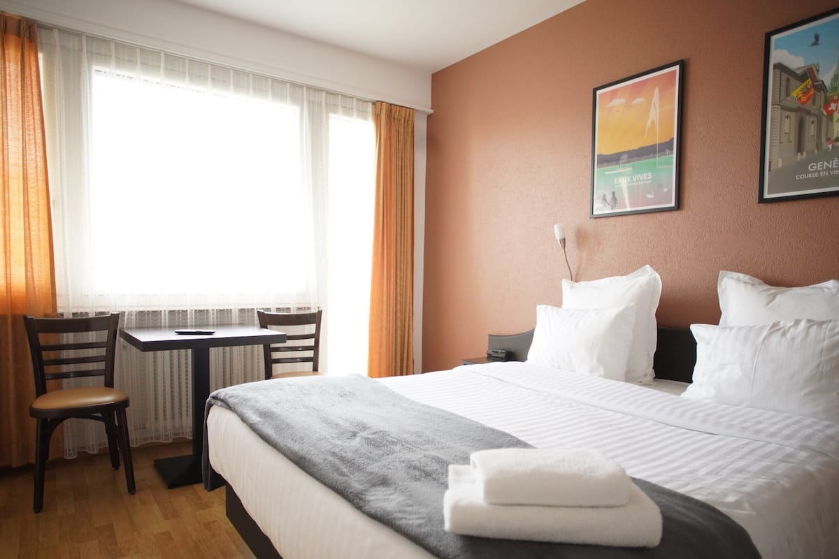 Habitación de hotel con cama, escritorio y silla. Hay dos ventanas con cortinas.