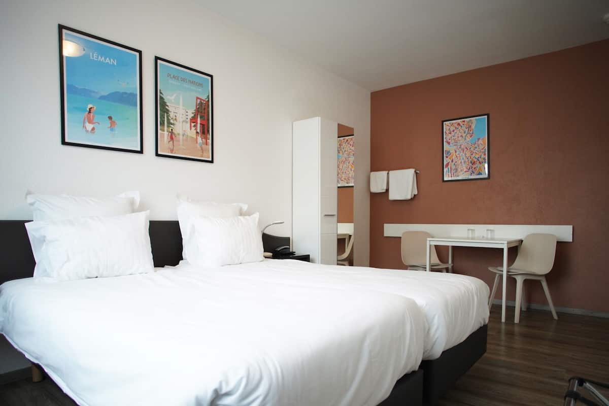 Habitación de hotel con una cama grande, un escritorio y dos sillas. Dos cuadros enmarcados adornan la pared.