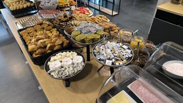 A buffet with various food items including pastries, cheeses, fruits, and condiments.
