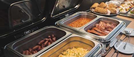 Un bufé con diversas opciones de comida, como frijoles, salchichas y huevos revueltos.