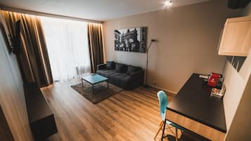 Una sala de estar moderna con un sofá, una mesa de centro y un escritorio con una silla. Hay un cuadro en la pared y una lámpara en el escritorio.