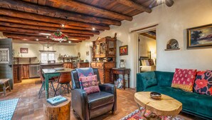 A rustic living room with a wooden ceiling, a green sofa, a leather armchair, and a dining area with a wooden table and chairs. - Authentic Santa Fe Home-Step into History & Charm (Santa Fe)