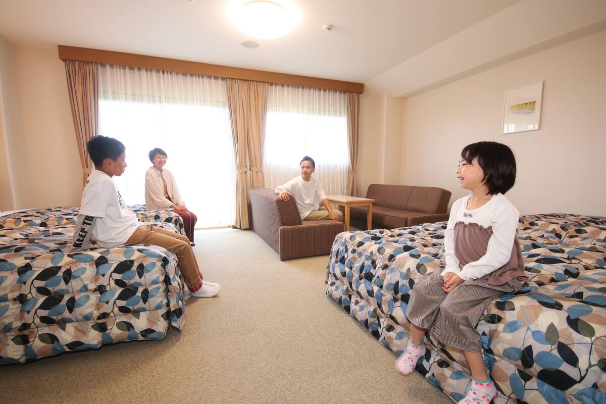 A hotel room with two beds, a sofa, a small table, and a window with curtains.
