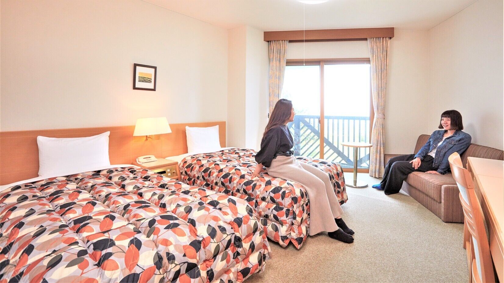 A hotel room with a large bed, a sofa, a small table, and a balcony.