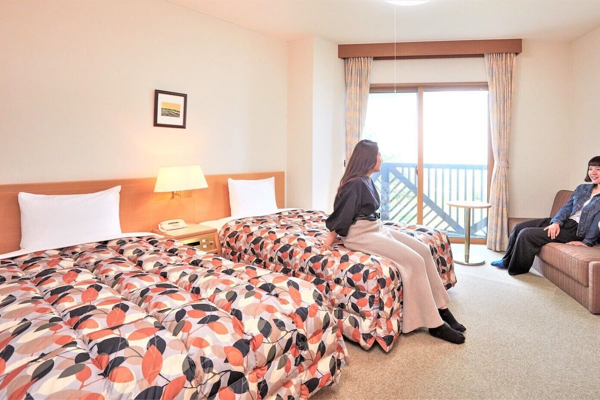 A hotel room with a large bed, a sofa, a small table, and a balcony.