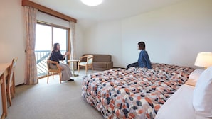 Habitación de hotel con cama, sofá, una mesita y una silla. Se ve una ventana con cortinas.