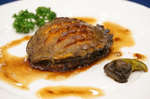 Un plato con pescado cocido, una verdura verde pequeña y salsa.
