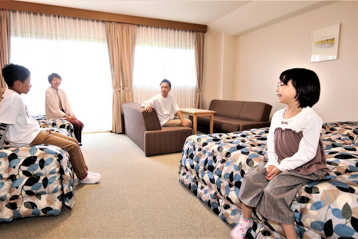 A hotel room with two beds, a sofa, a small table, and a window with curtains.
