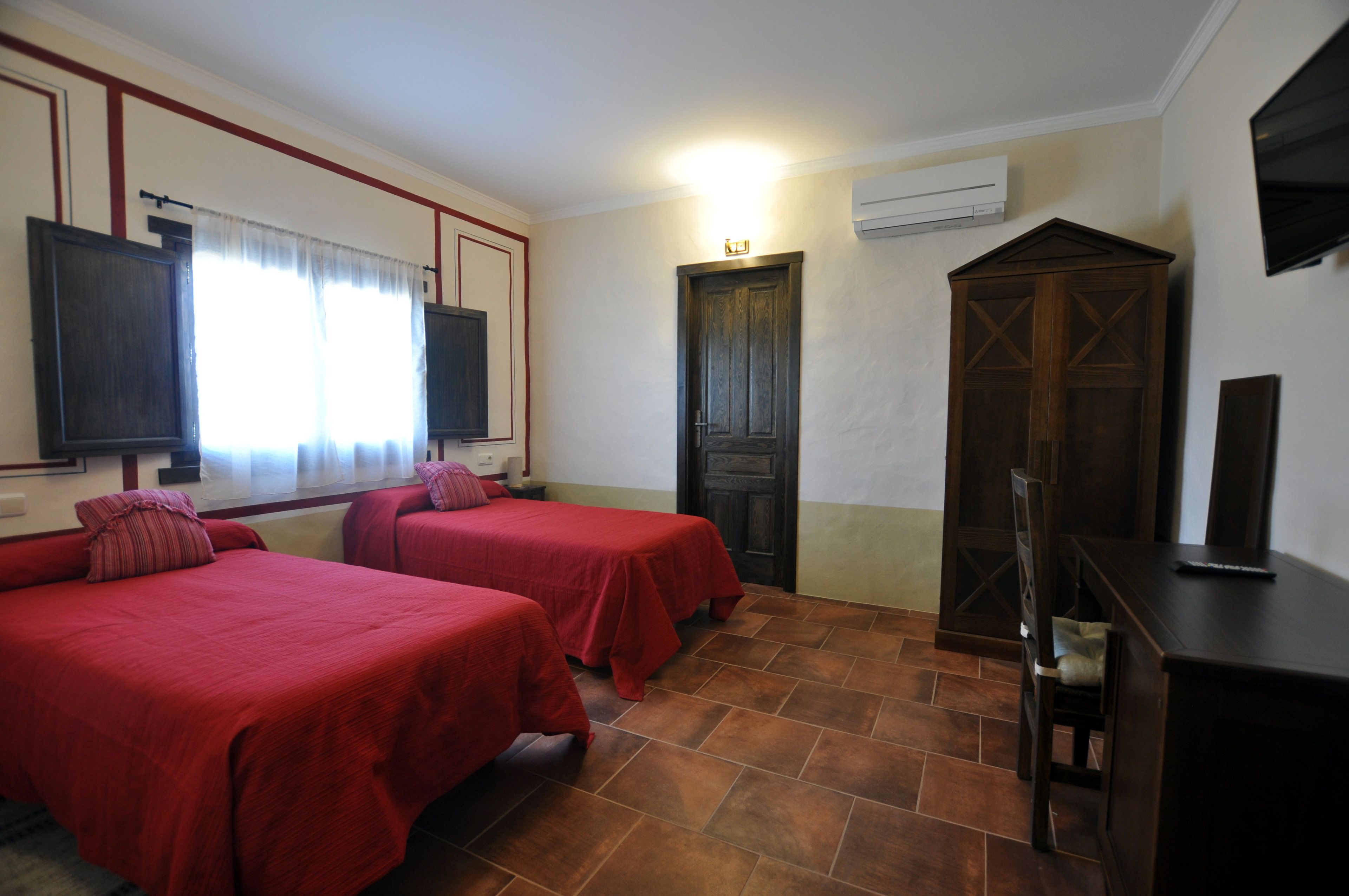 A hotel room with two single beds, a wooden wardrobe, a television, and an air conditioning unit.