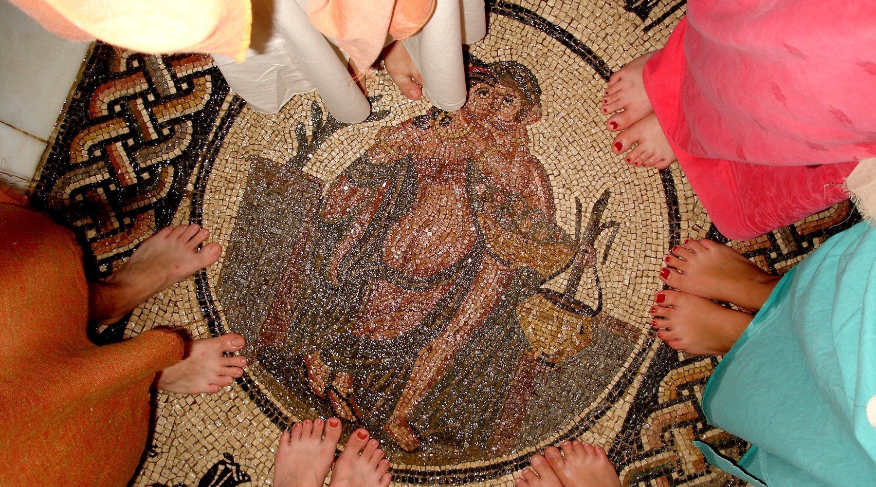 A mosaic floor with a central figure surrounded by people standing around it.
