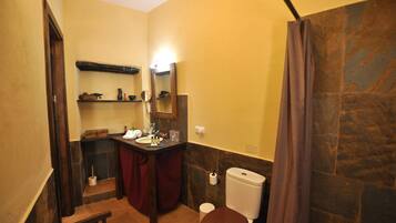 A bathroom with a wooden bench, a toilet, a sink with a mirror, and a shelf with toiletries.