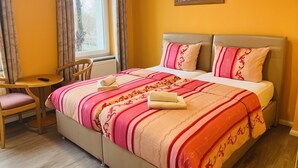Una camera d'albergo con un letto, una sedia, un tavolino e un quadro appeso al muro.