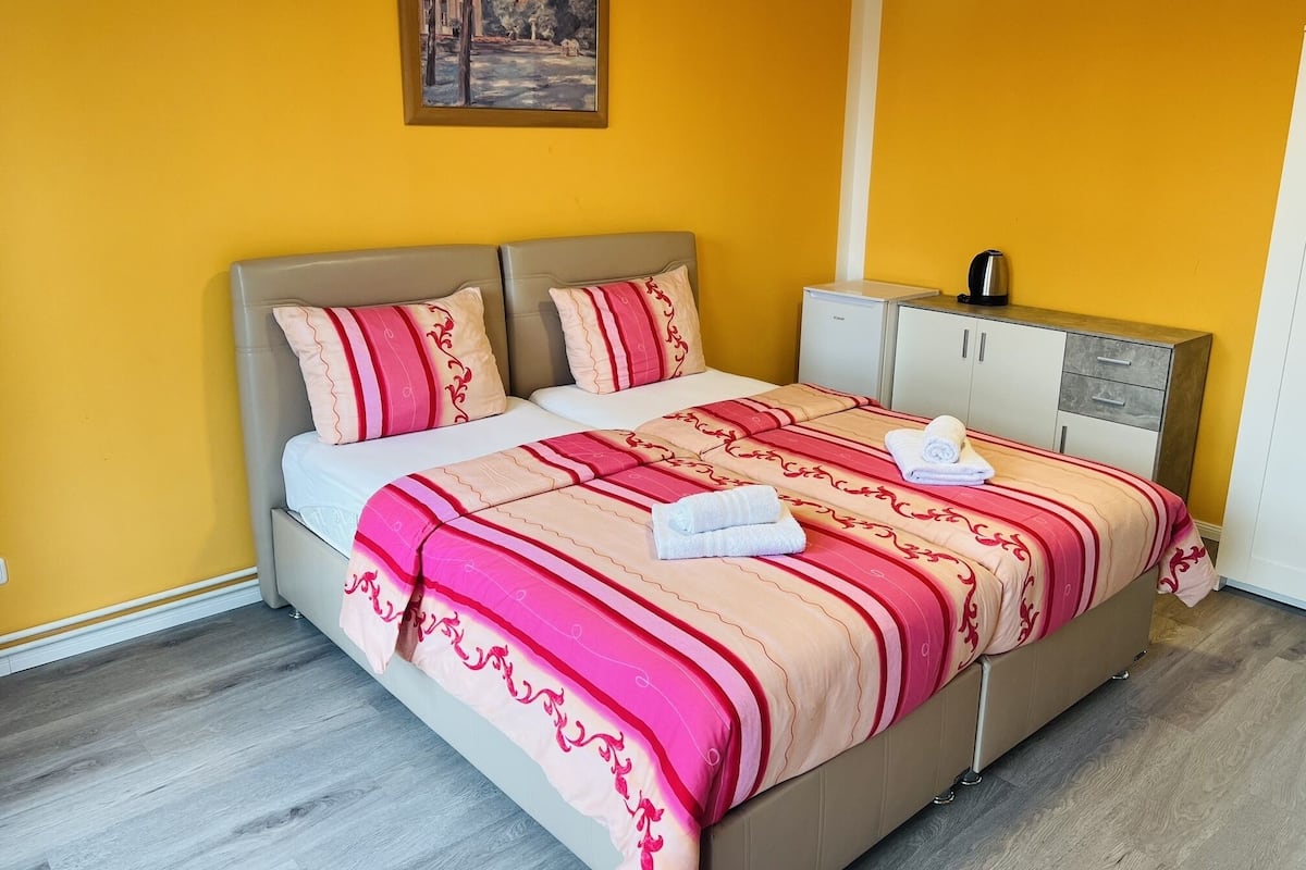 Een hotelkamer met een bed, nachtkastje, klein kastje en een schilderij aan de muur.