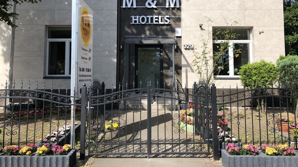 L'ingresso di un hotel con un cancello in ferro battuto, una targa e un'aiuola curata.
