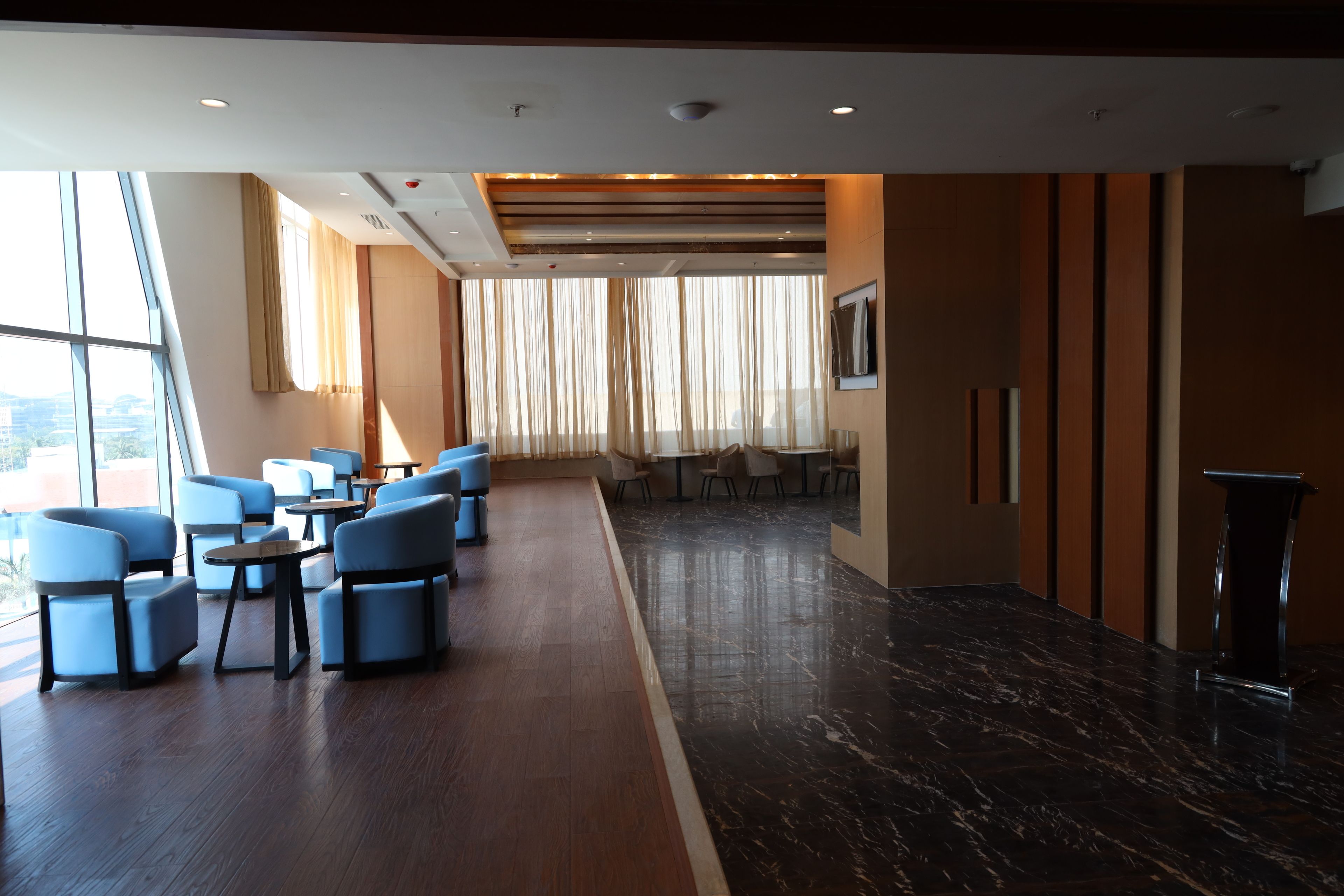 Un moderno vestíbulo de hotel con zona de estar, mostrador de recepción y grandes ventanales con cortinas.