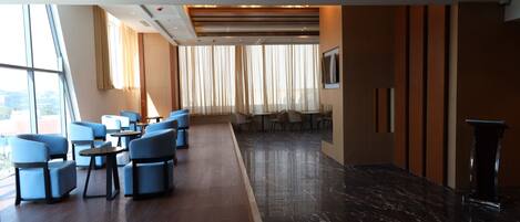 Un moderno vestíbulo de hotel con zona de estar, mostrador de recepción y grandes ventanales con cortinas.