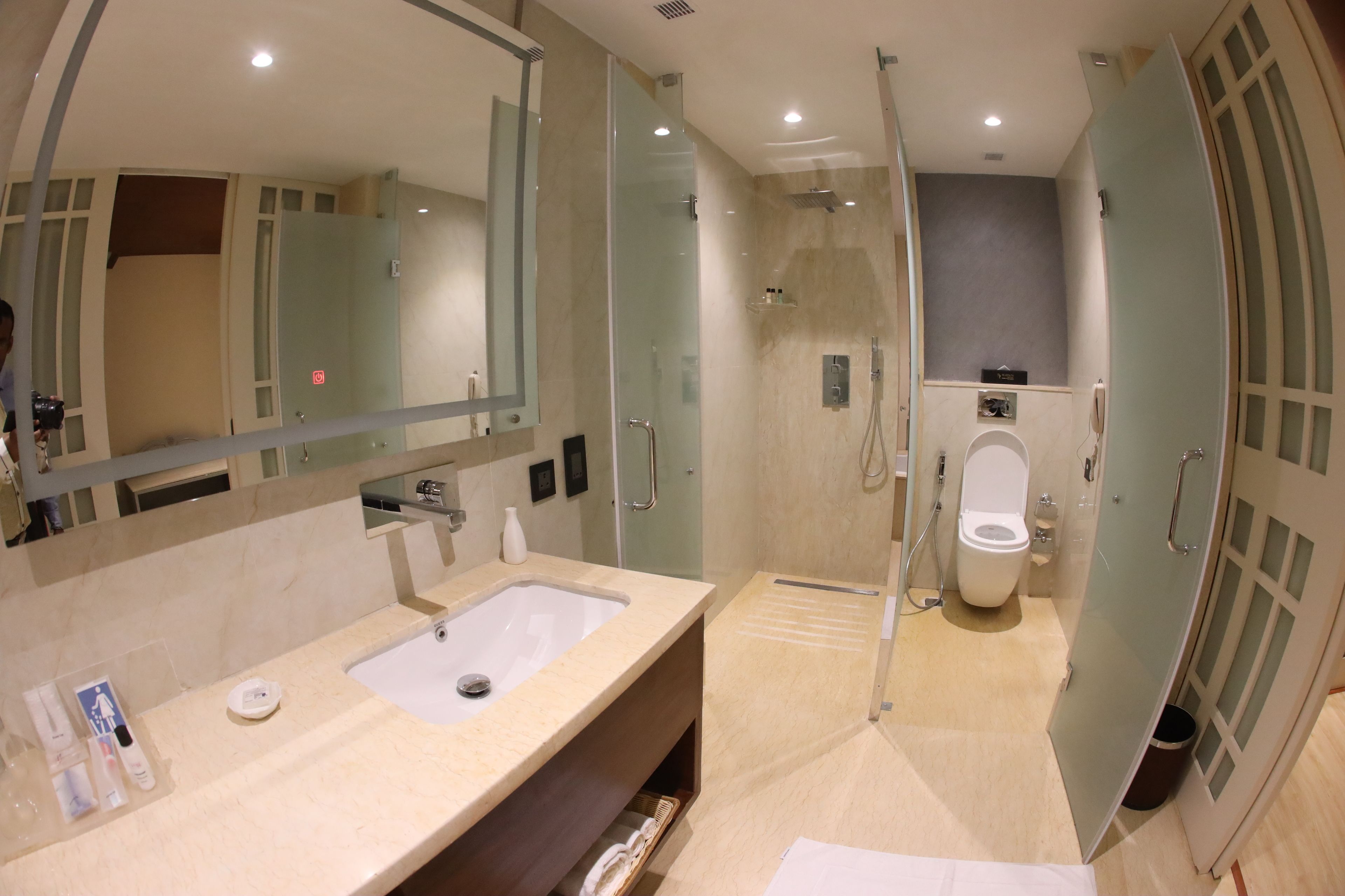 A modern bathroom with a large mirror, a sink, a shower, and a toilet.