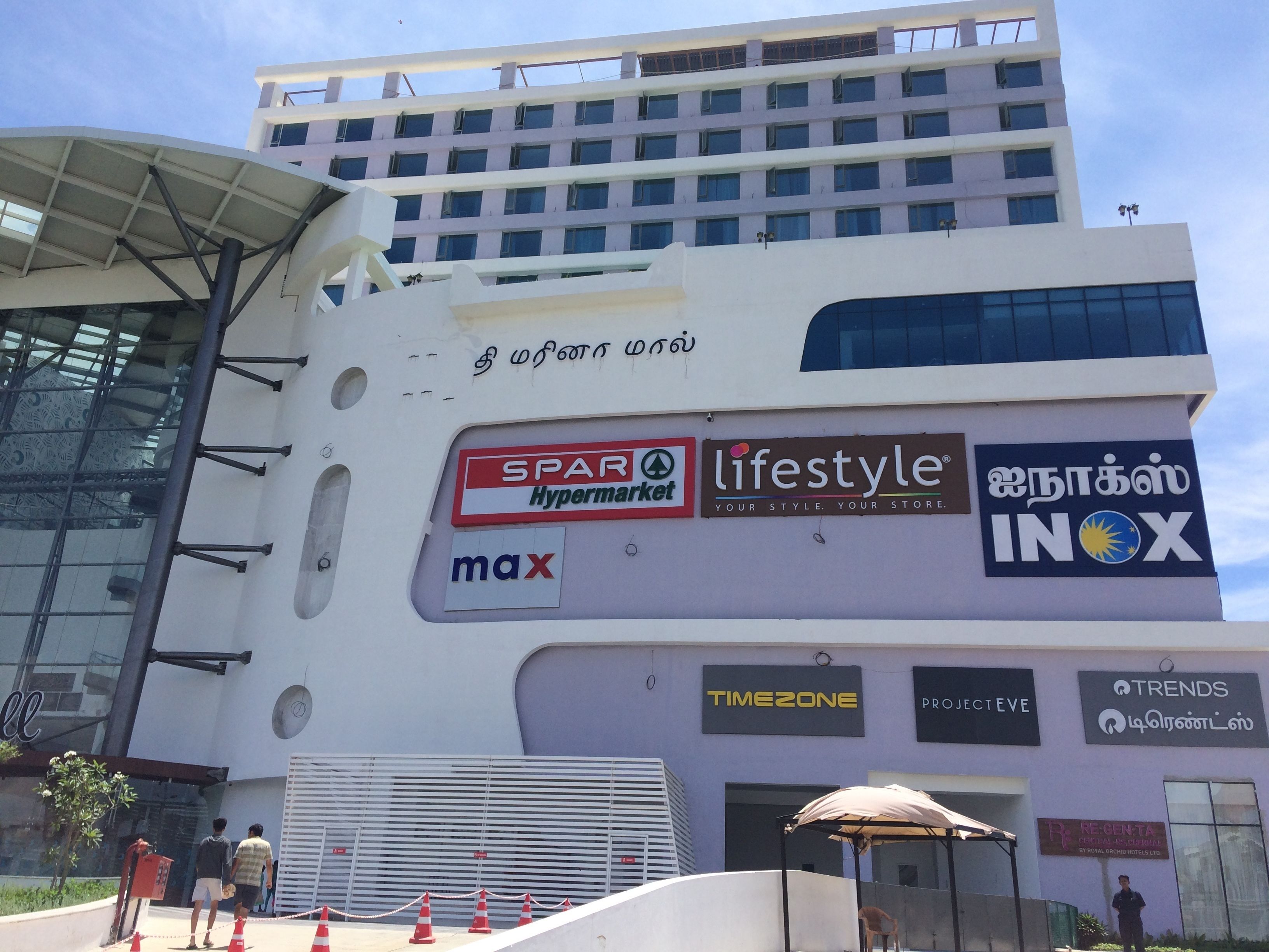 Un edificio de varios pisos con diversos rótulos comerciales, incluyendo 'SPAR Hypermarket', 'lifestyle', 'max', 'INOX', 'TIMEZONE', 'PROJECT EVE' y 'RE-GEN-TA'.