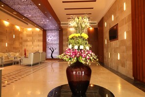 A lobby with a large vase of flowers on a round table, a seating area with sofas, and a patterned wall. - Regenta Central RS - Chennai (Tirupporur)