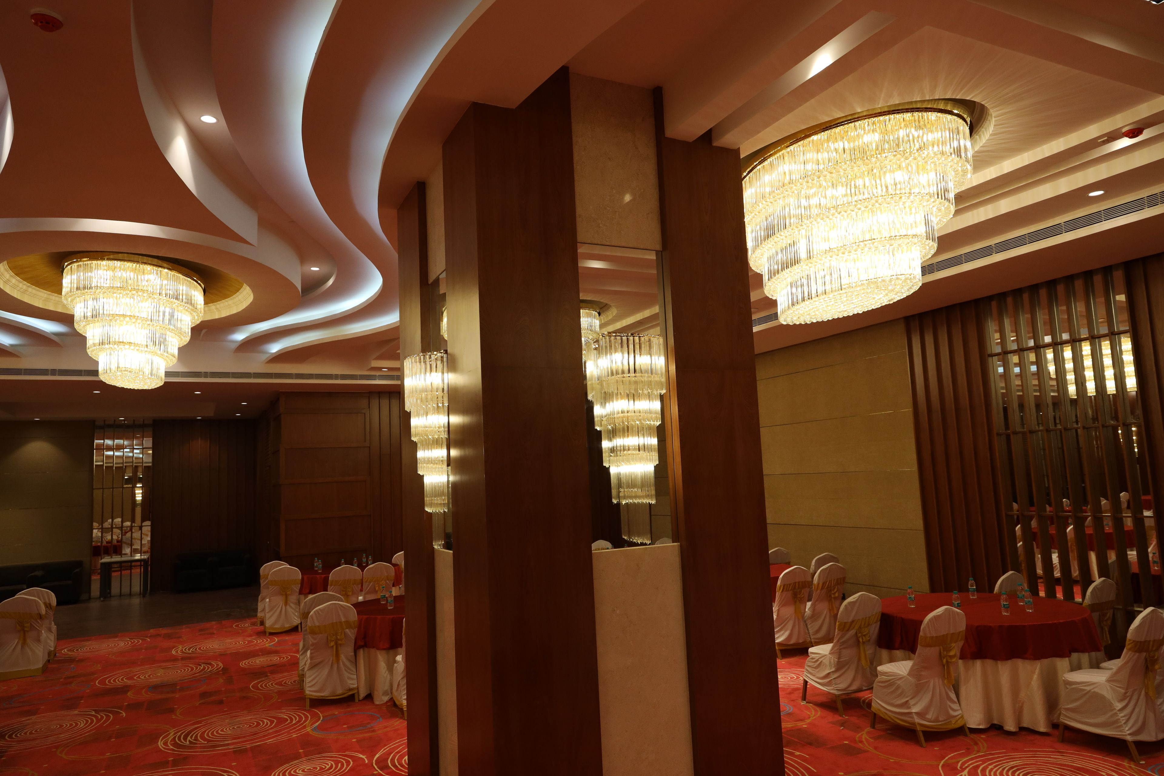 A banquet hall with round tables, white chairs, and chandeliers.